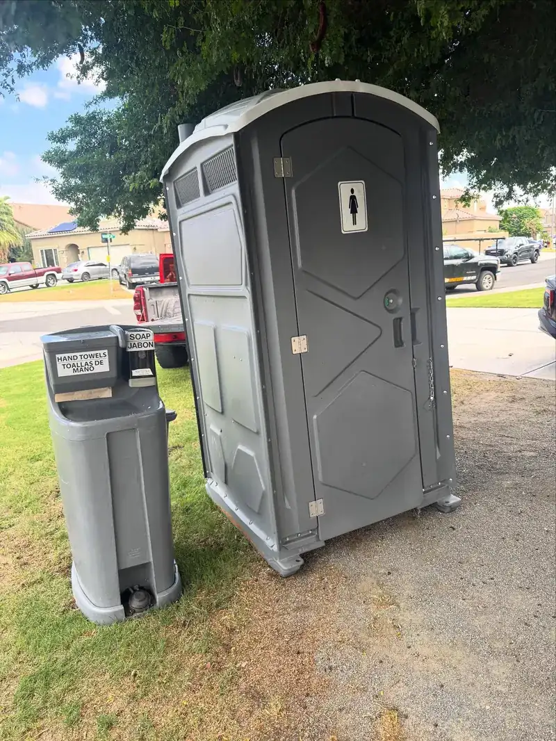 Grey deluxe porta potty with a handwashing station on grass